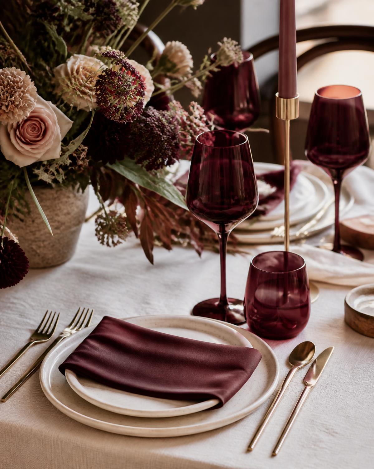 Mise en place elegante con lino panna, calici bordeaux e composizione floreale